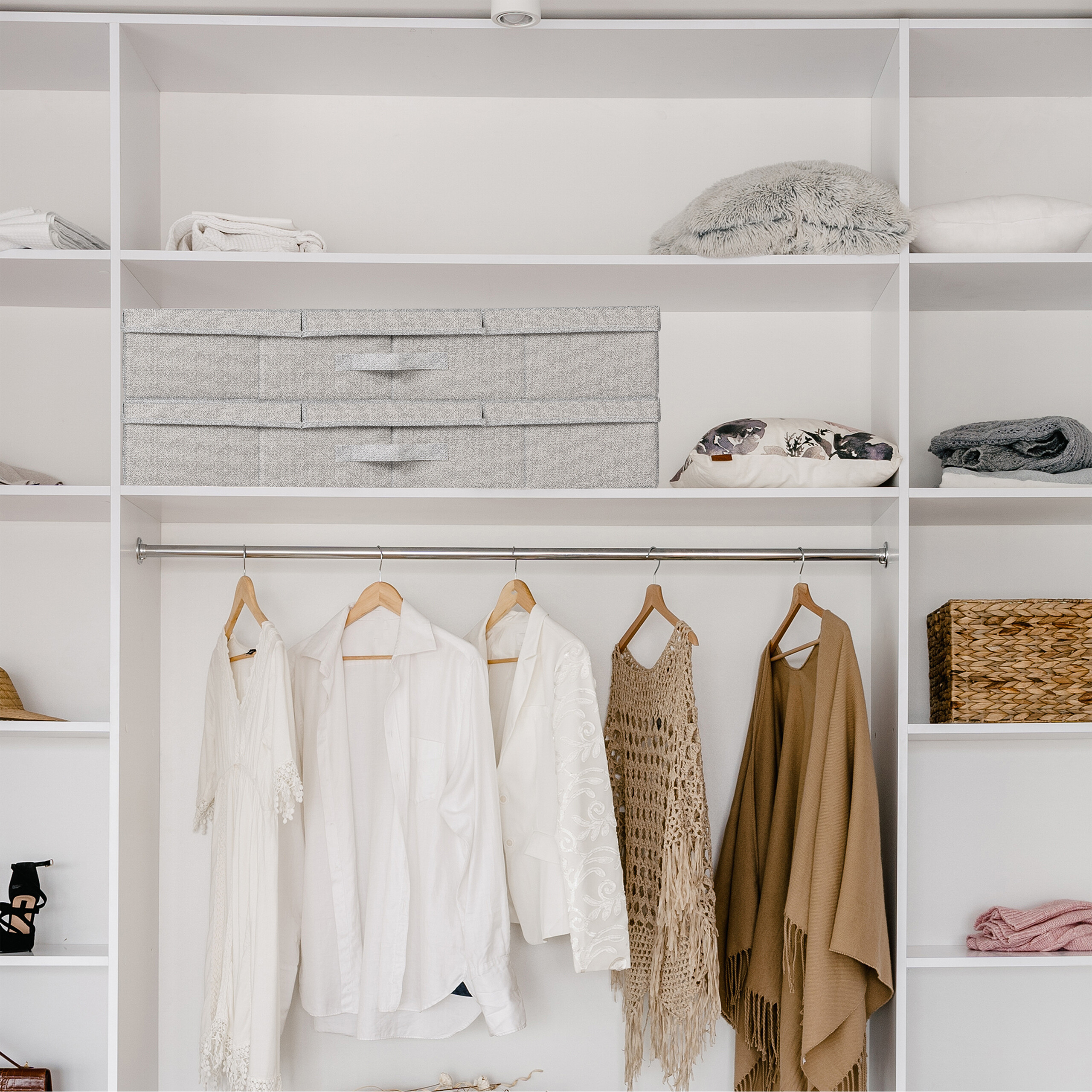 Ein weißer Kleiderschrank mit Regalen, Kissen und aufgehängter Kleidung.