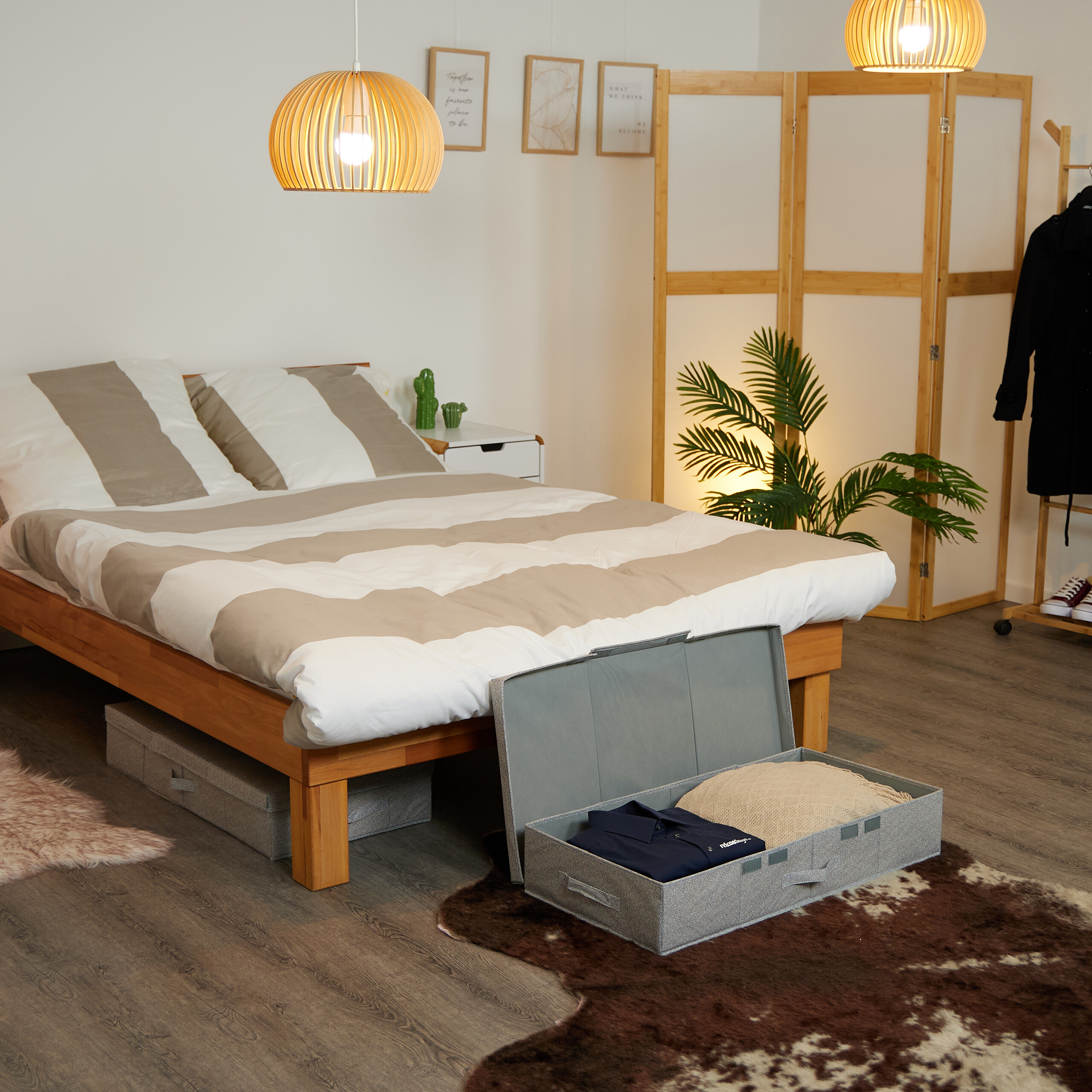 Ein Schlafzimmer mit einem Holzbett, braunem Teppich und einer geöffneten grauen Aufbewahrungsbox mit Kleidung.