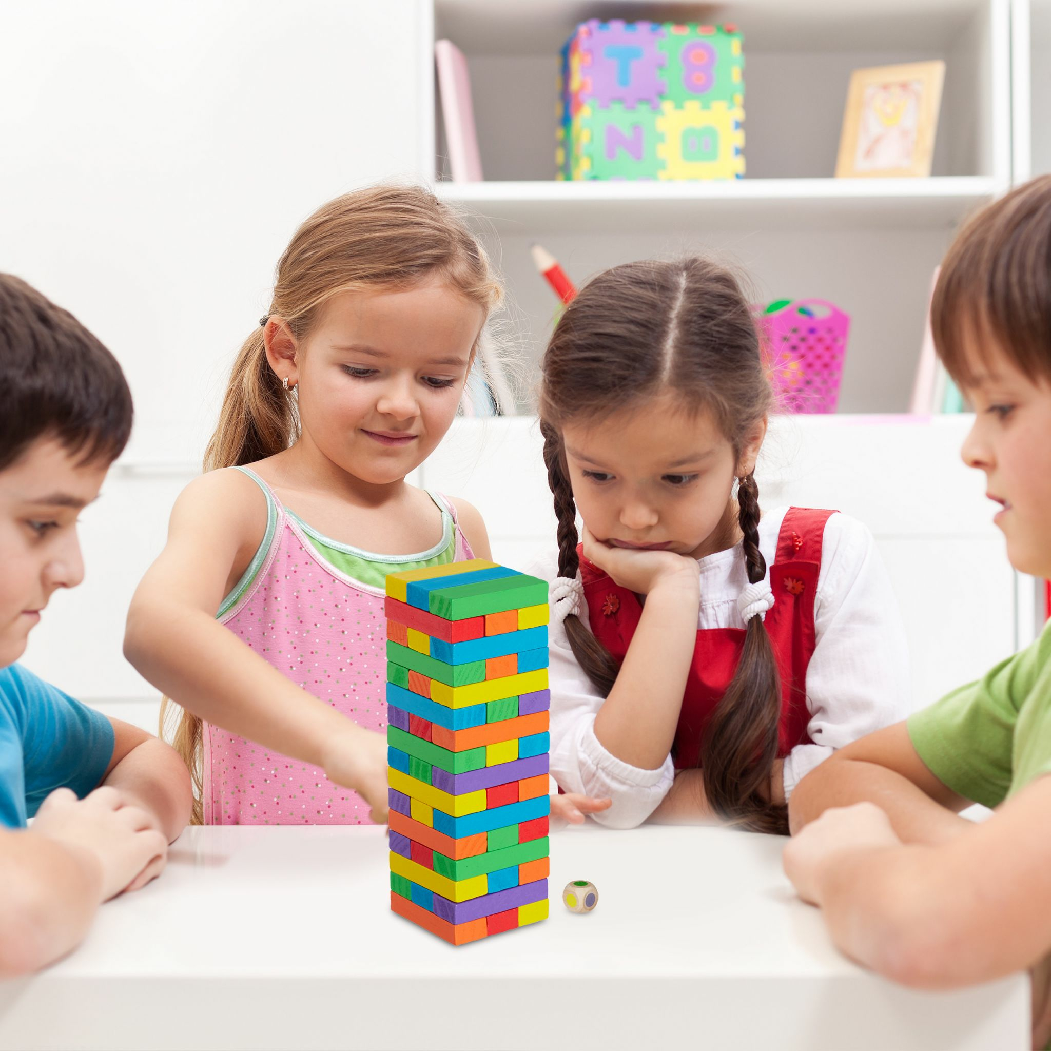 Vier Kinder spielen an einem weißen Tisch zusammen und bauen einen bunten Holzturm.