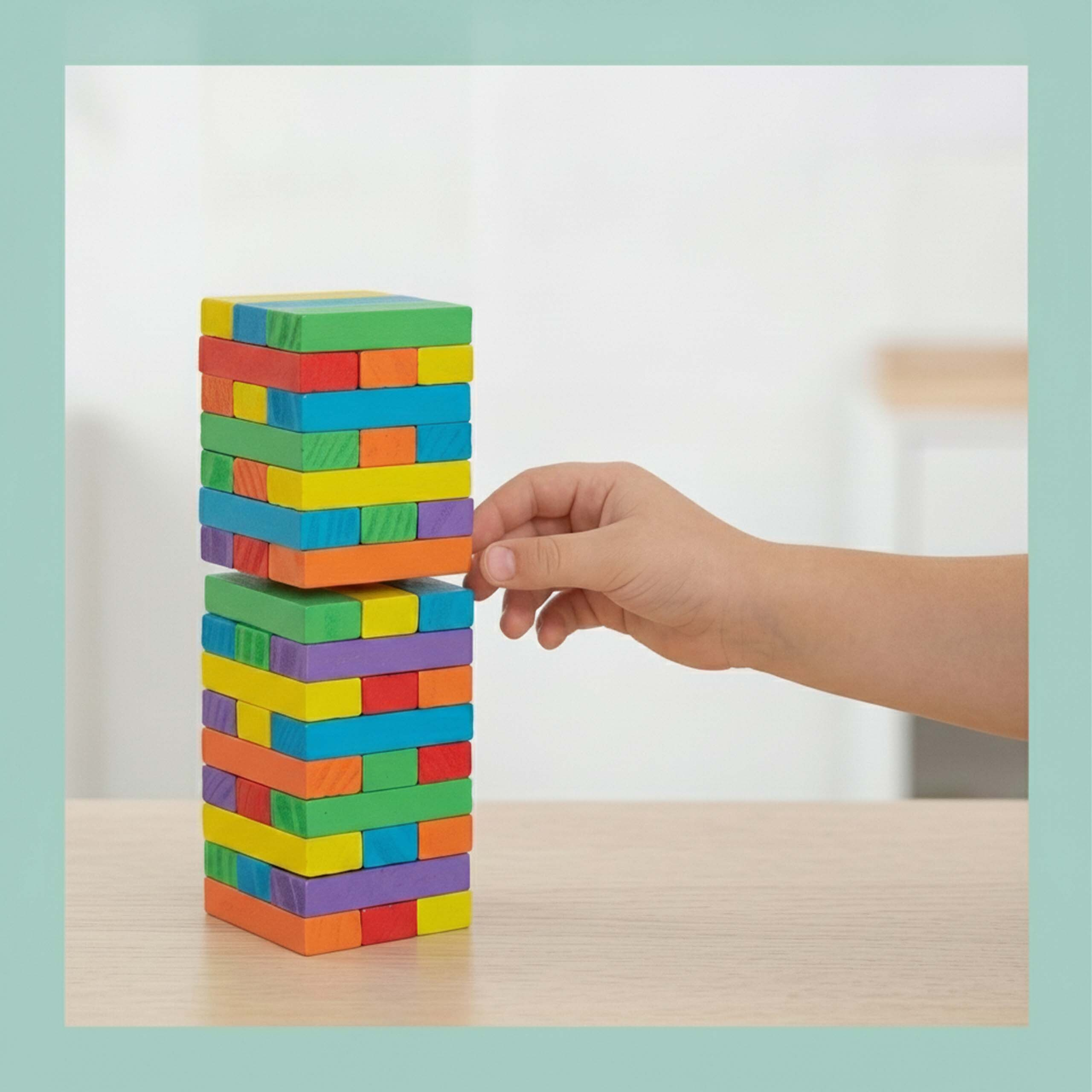 Ein Kindersarm zieht vorsichtig einen bunten Holzklotz aus einem Turm auf einem Holztisch.