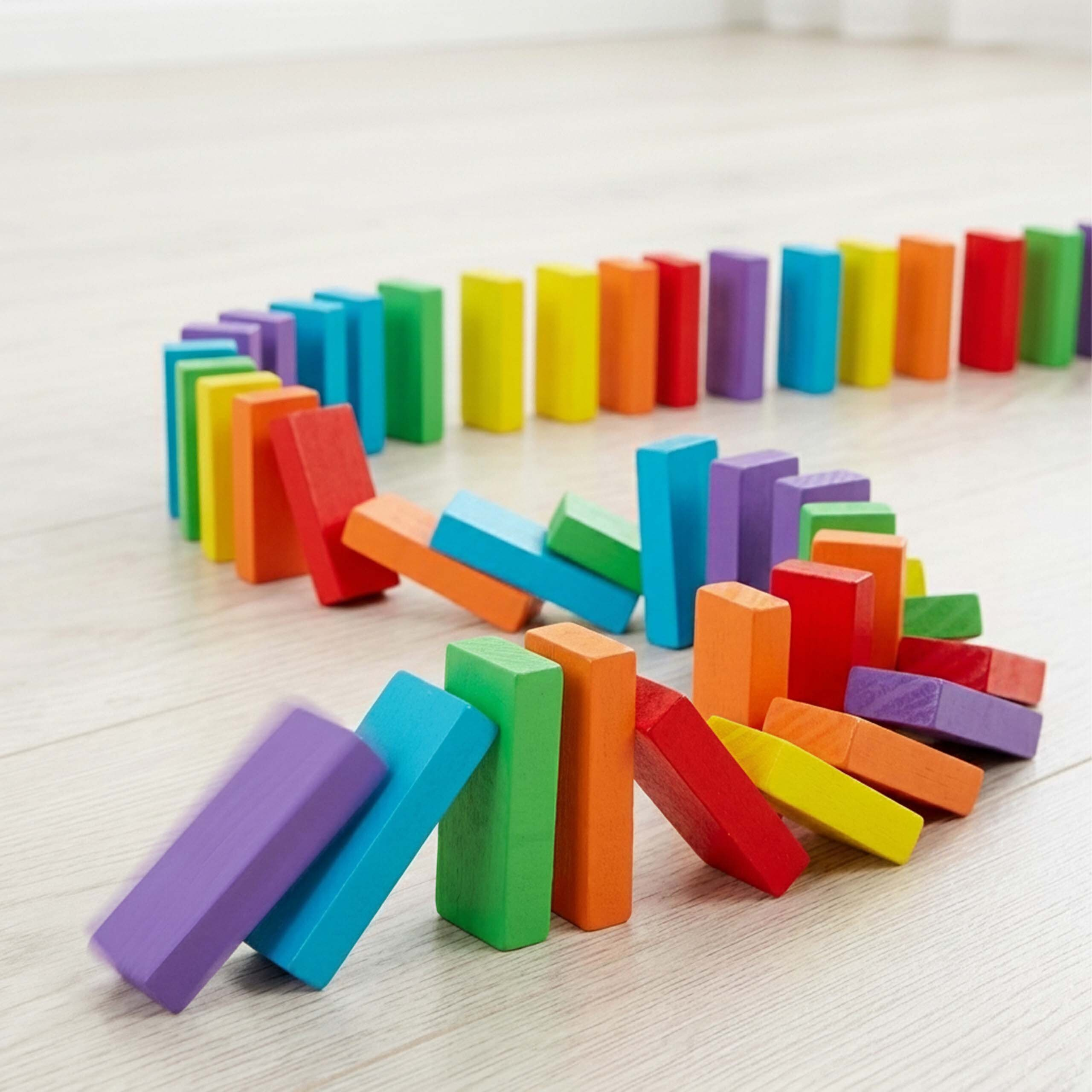 Bunte Holzdokinos fallen in einer geschwungenen Linie auf hellem Holzboden um.