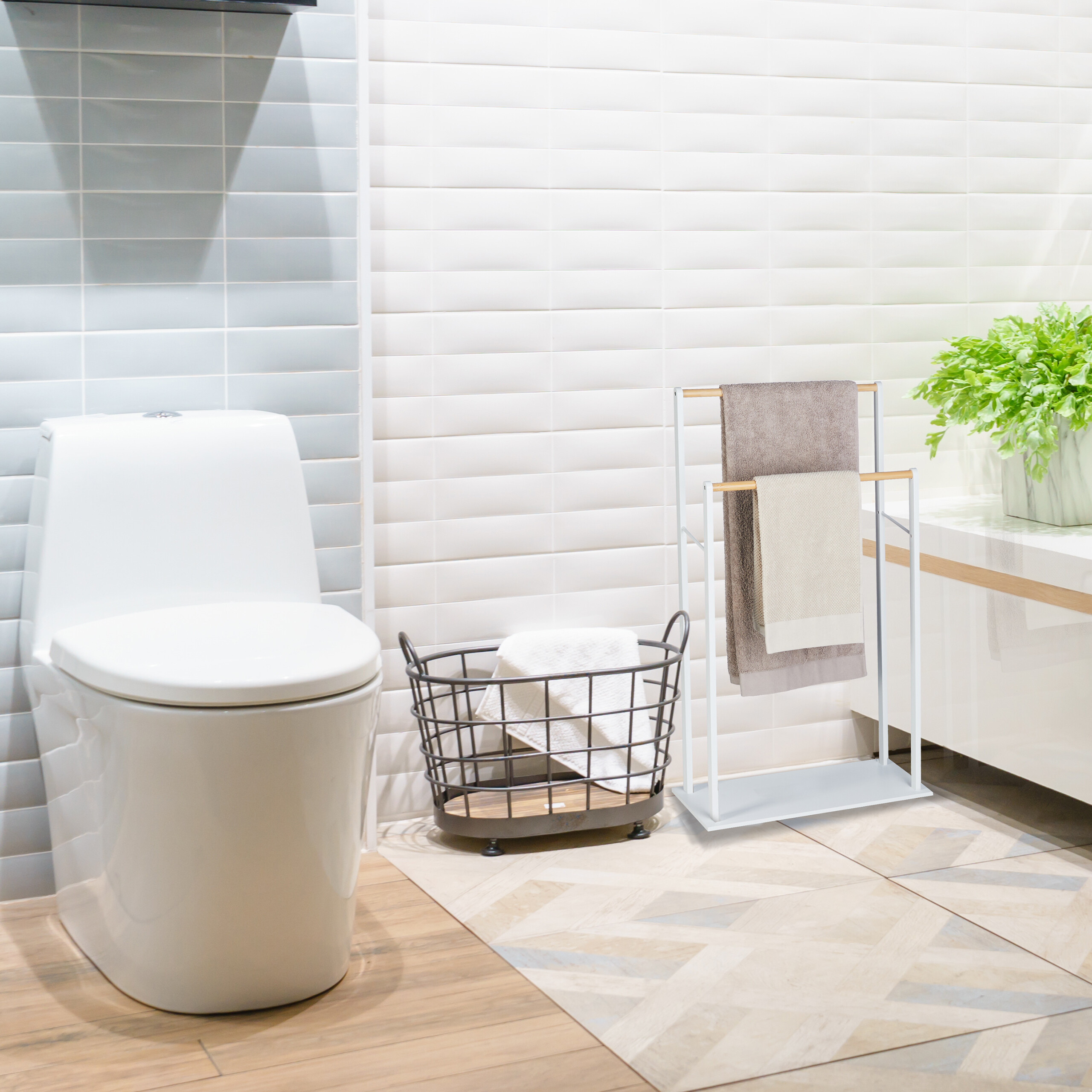 Ein modernes Bad hat eine weiße Toilette, einen Drahtkorb mit Handtuch, einen Handtuchhalter und eine Pflanze.