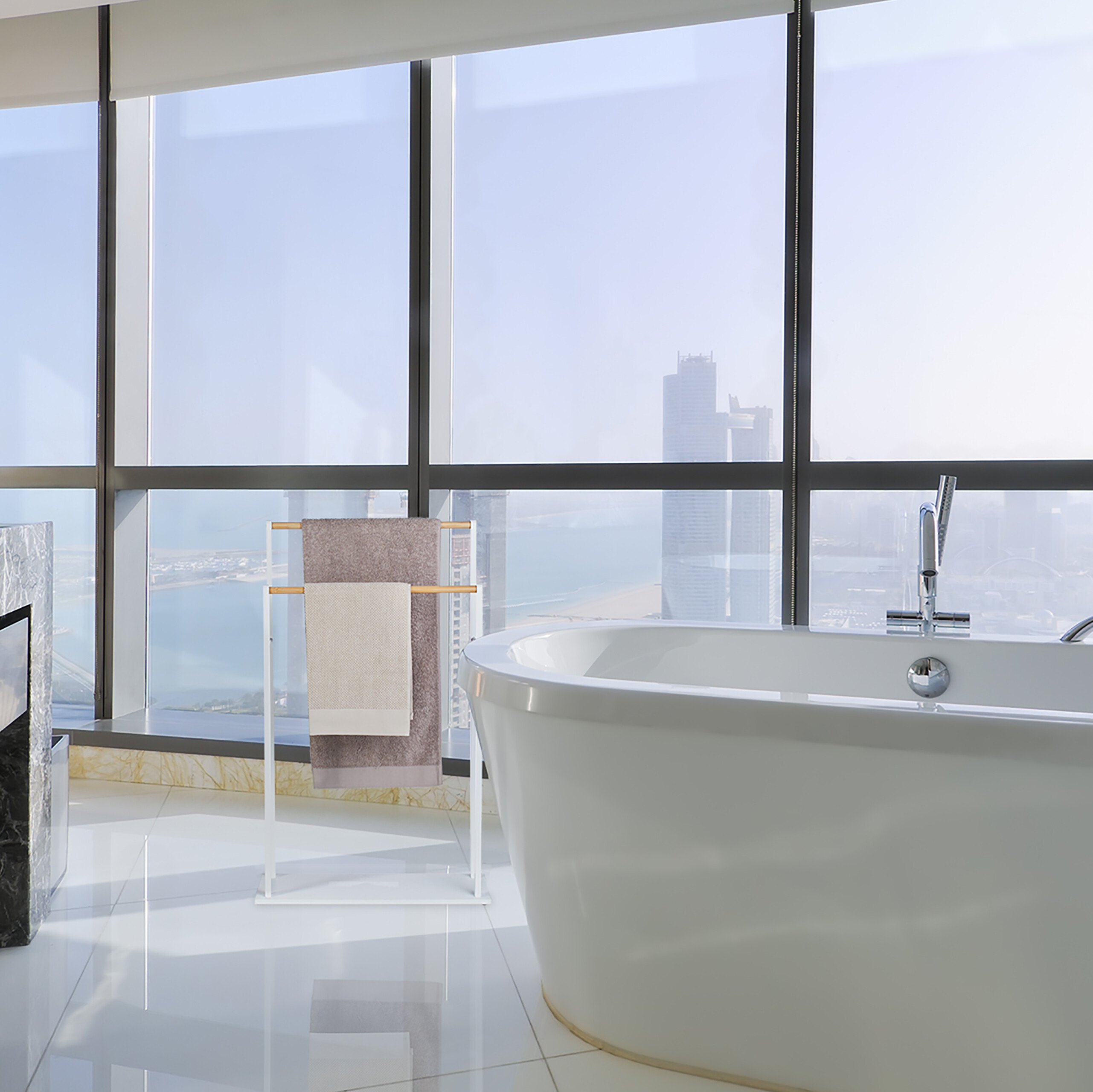 Eine moderne weiße Badewanne in einem Luxusbad mit großen Fenstern und Blick auf die Skyline und das Meer.