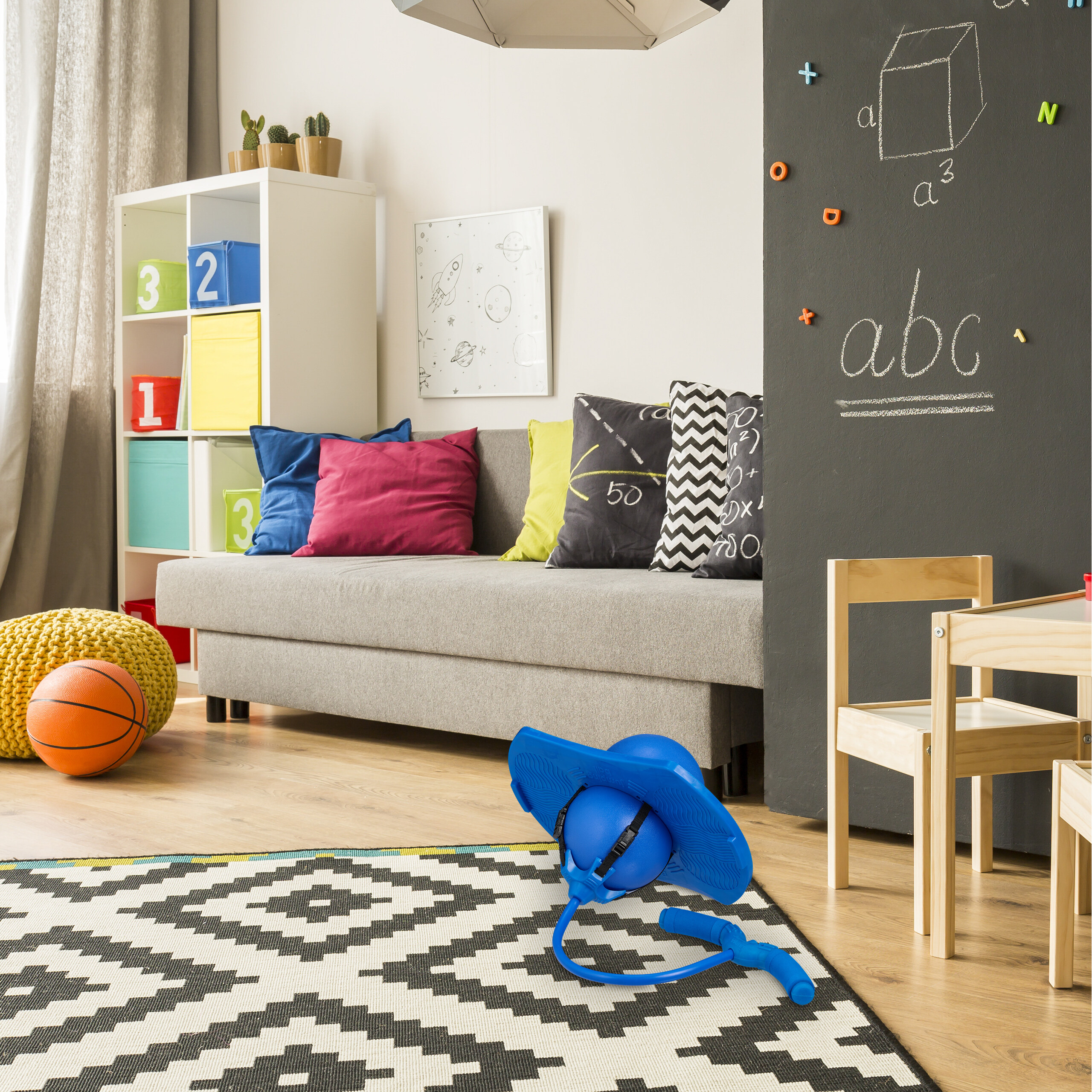 Ein Kinderzimmer hat ein graues Sofa, ein weißes Regal mit bunten Boxen, eine Tafelnwand und Spielzeug.