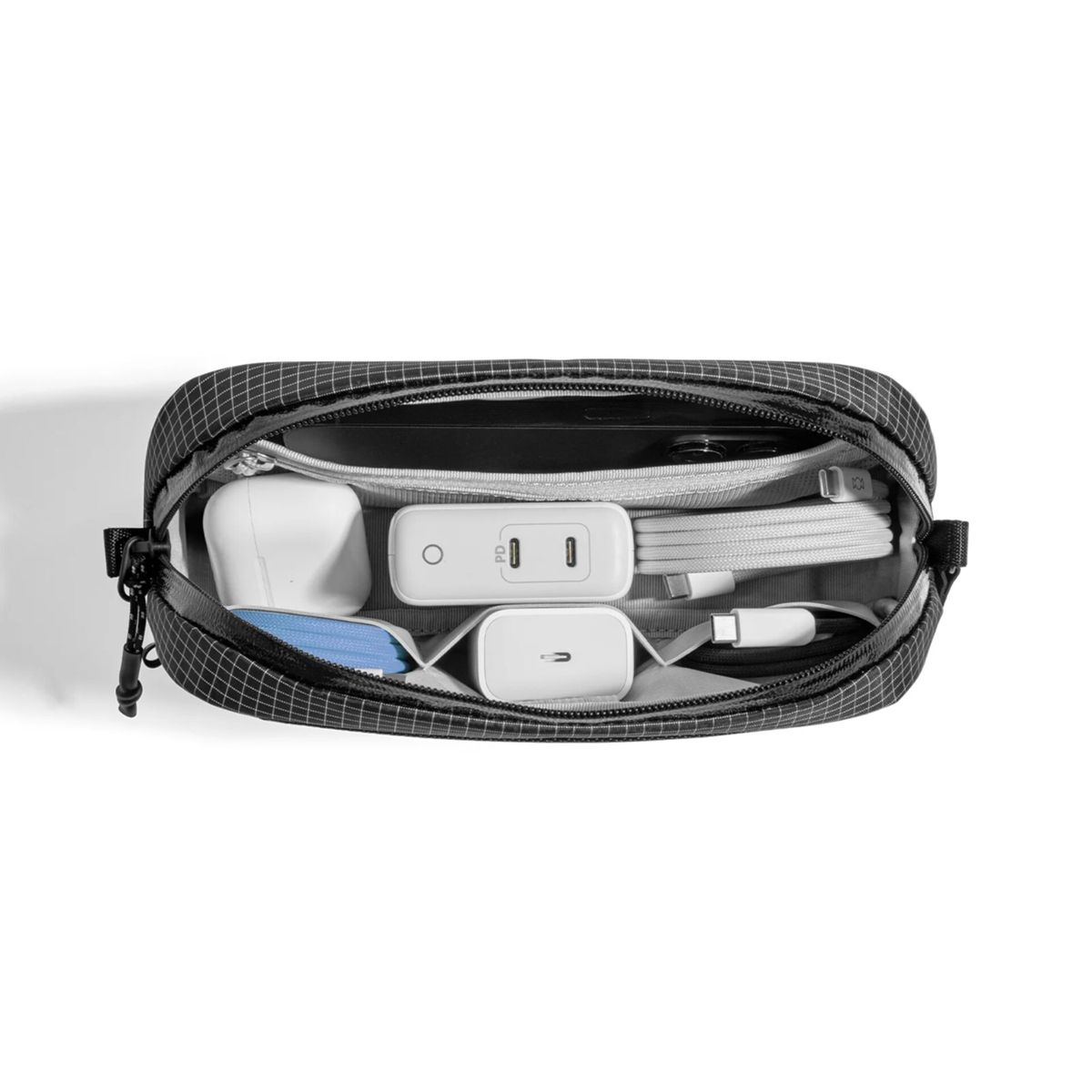 Eine offene schwarze Tasche mit Gittermuster enthält weiße Ladegeräte, USB-Kabel und Ohrhörer.