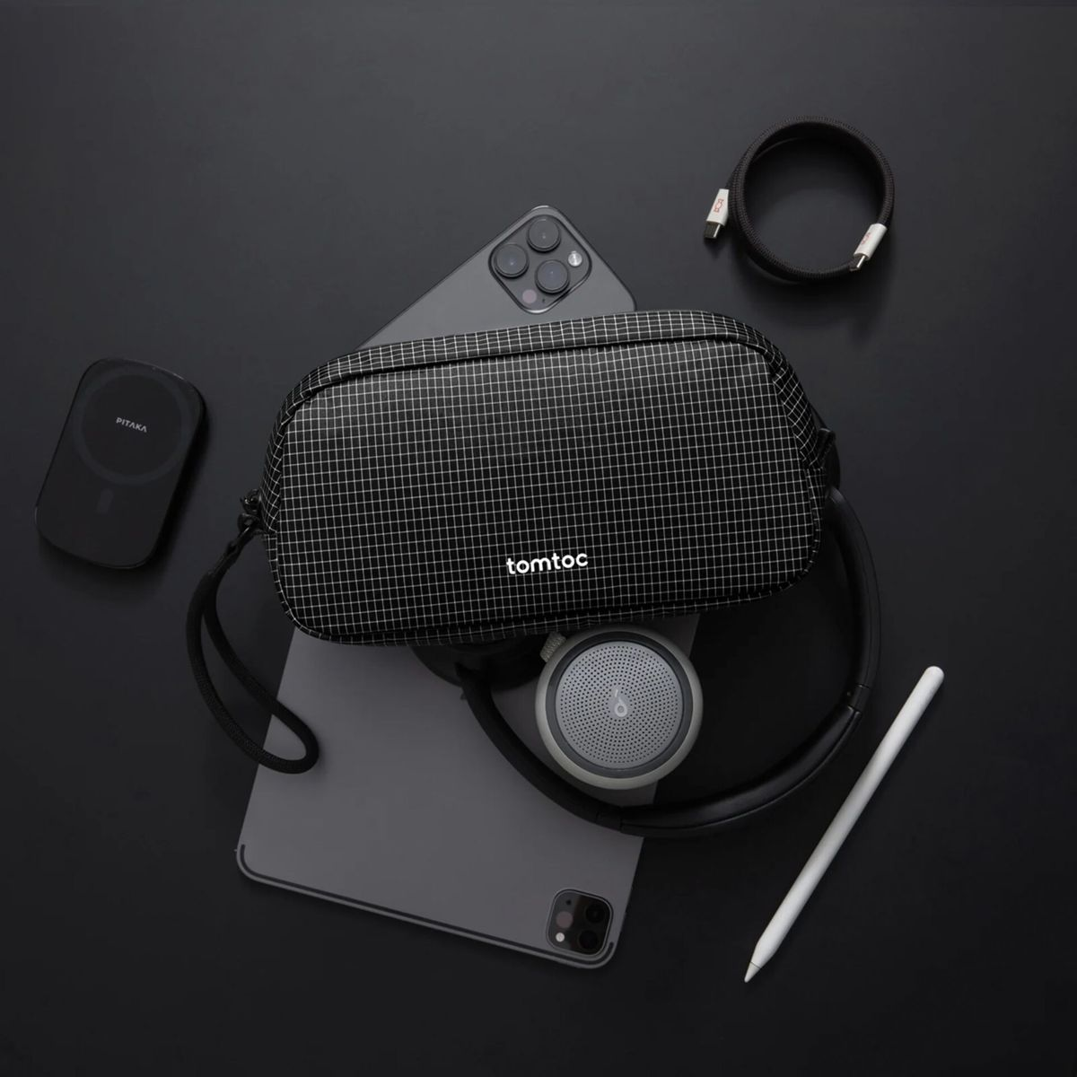 Flachlay-Ansicht mit einer schwarz-weißen Tomtoc-Tasche, einem Tablet, Kopfhörern, einem Stift und Zubehör.