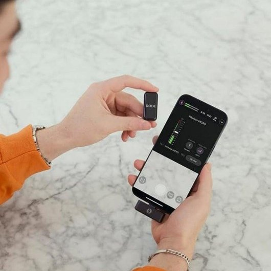 Una mano tiene un piccolo microfono e l'altra uno smartphone con un ricevitore collegato.