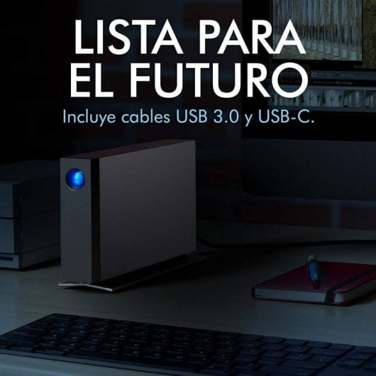 Hard disk esterno nero con pulsante blu su scrivania con tastiera, taccuino e monitor.