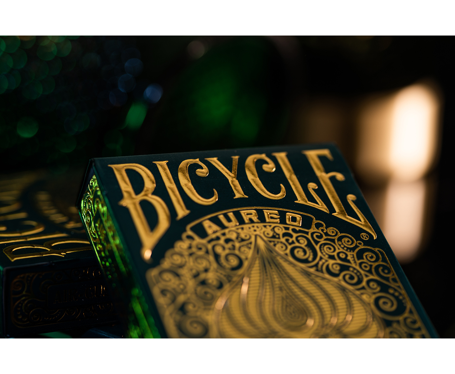 Eine grüne Bicycle Aureo Spielkartenbox mit goldenem Prägemuster vor verschwommenem Hintergrund.