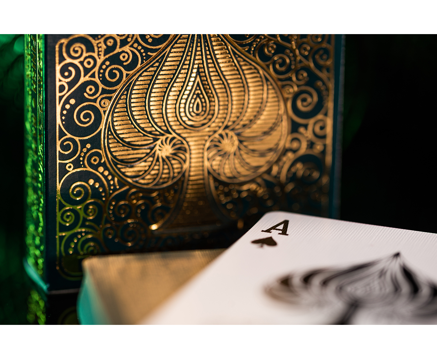 Goldene Ornamentik auf einer dunklen Spielkartenbox mit einem Pik-Ass davor.