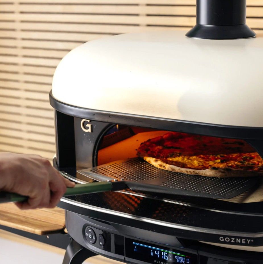 Eine Hand schiebt eine Pizza auf einem Lochblech in einen modernen Gozney-Pizzaofen.
