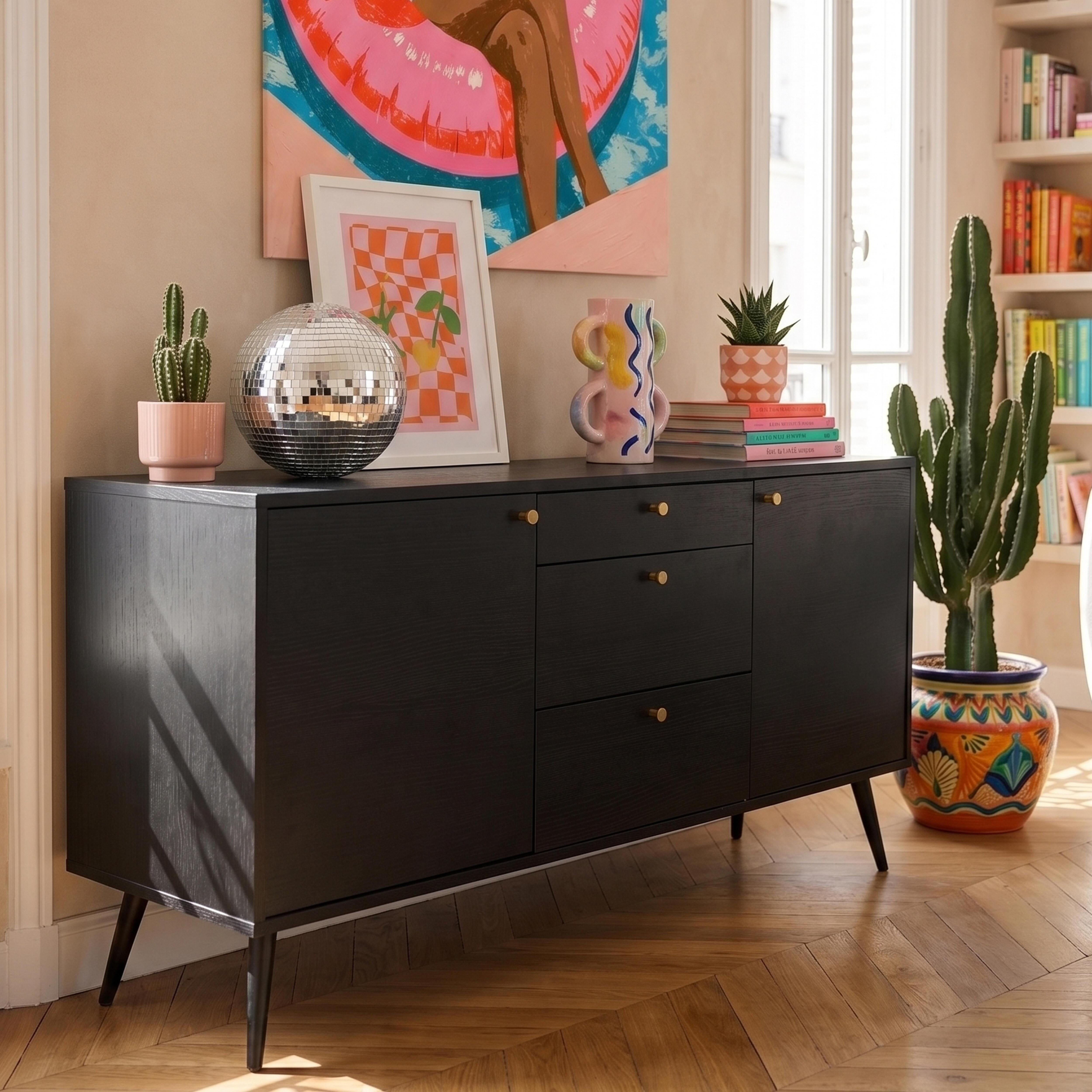 Ein schwarzes Sideboard mit Kunst, Discokugel und Kakteen auf Holzboden.