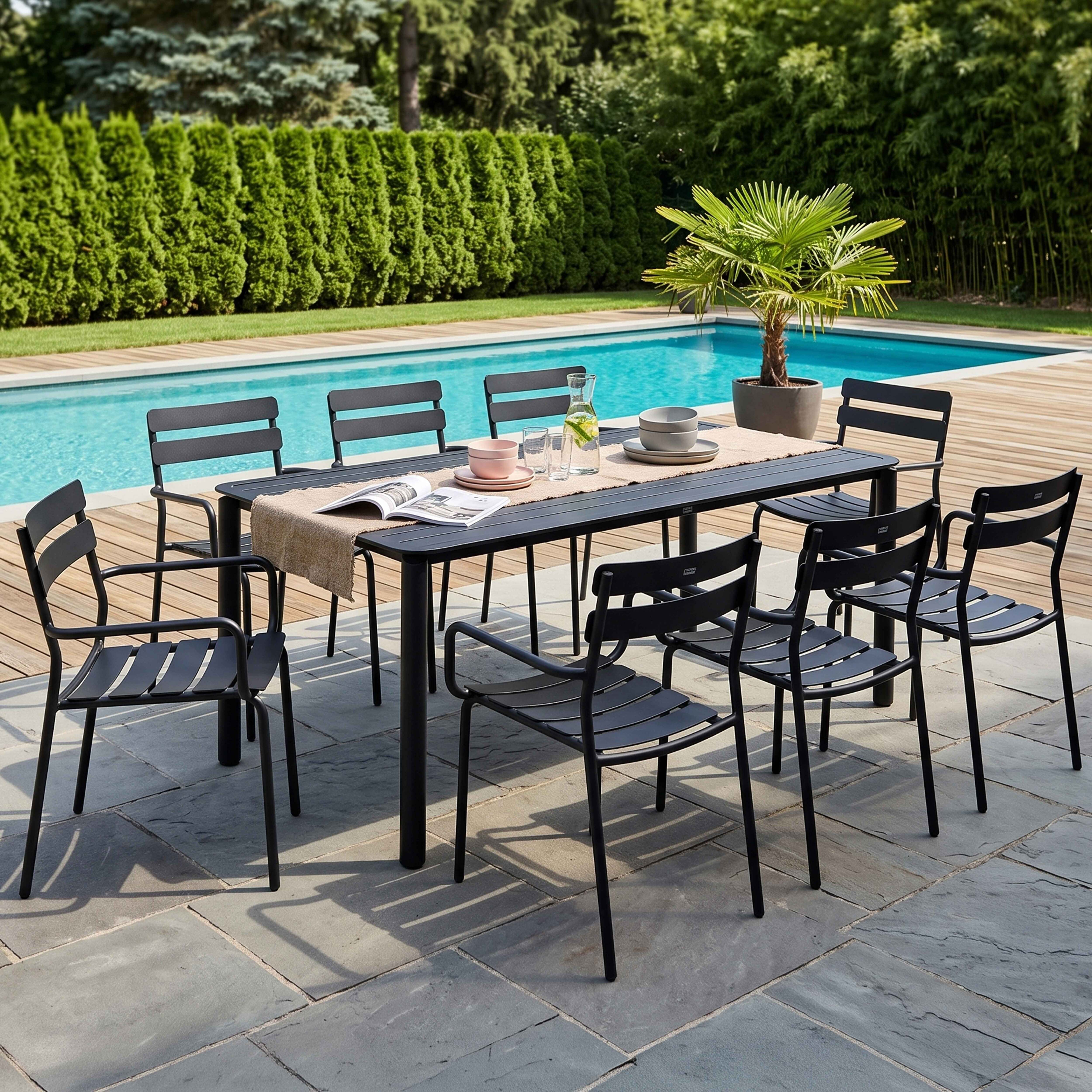 Ein schwarzer Tisch und passende Stühle stehen auf einer Steinterrasse am Pool im Garten.