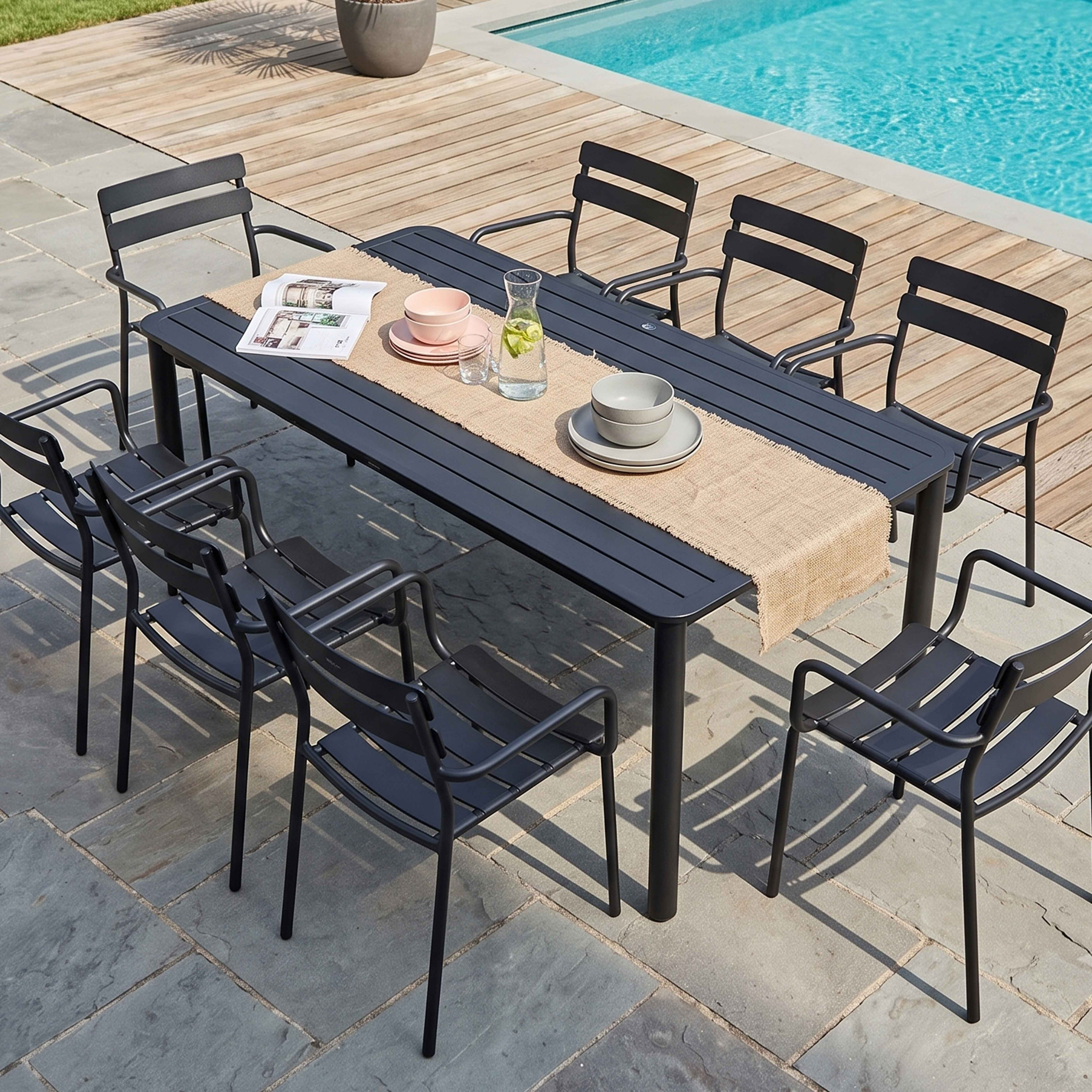 Ein grauer Gartentisch mit Stühlen steht auf einer Terrasse neben einem Swimmingpool.