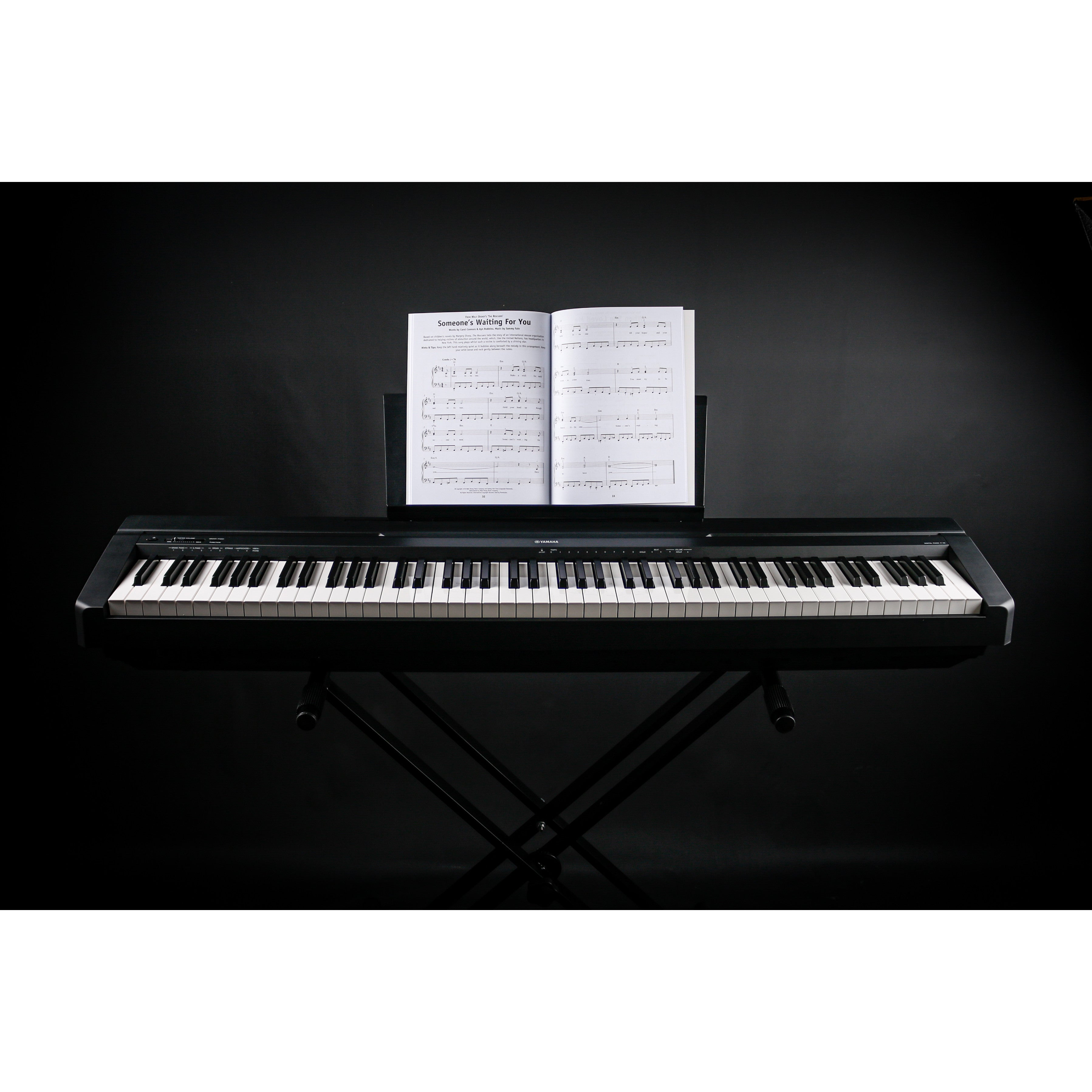 Ein schwarzes Digitalpiano auf einem Ständer mit Notenblättern auf dem Notenpult vor schwarzem Hintergrund.