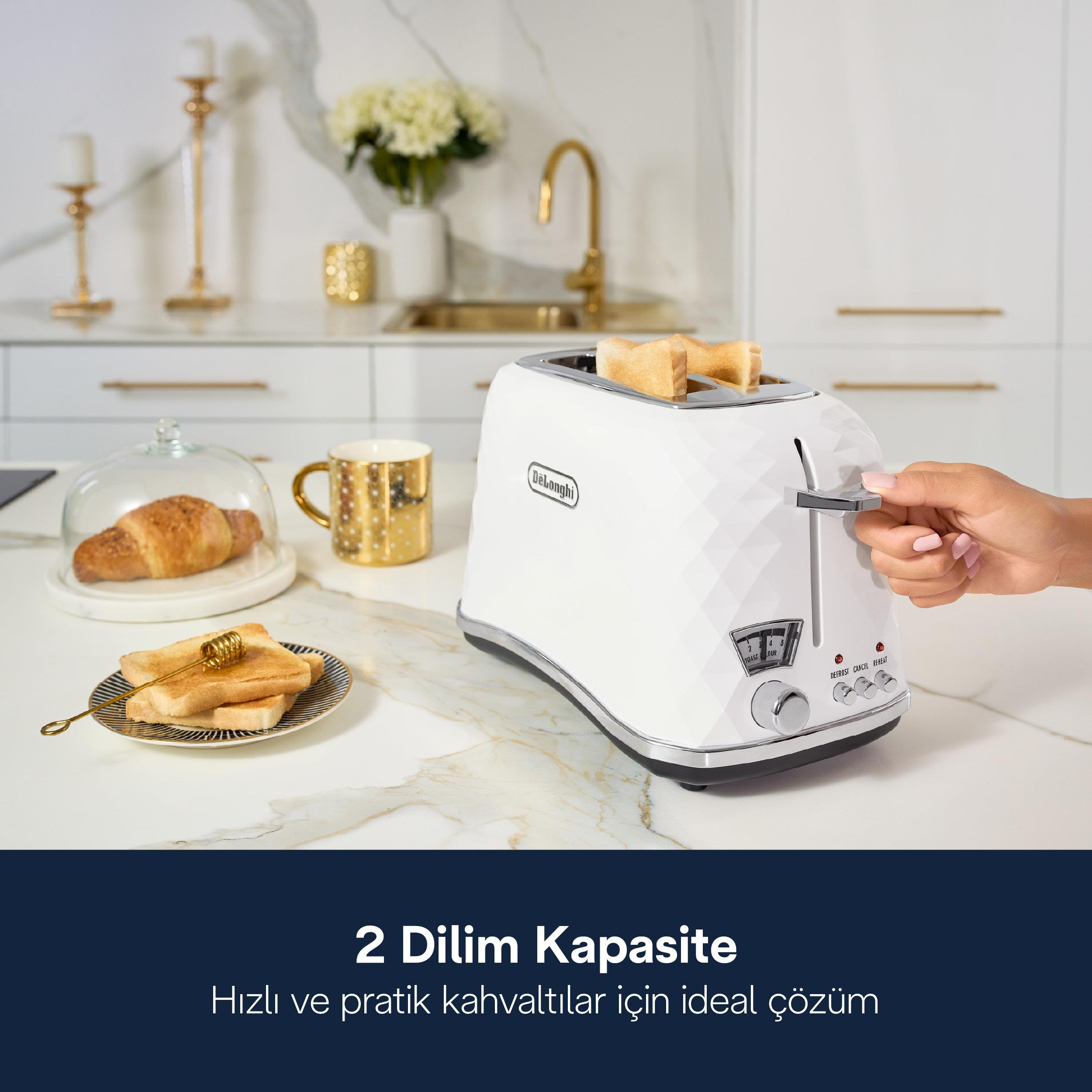 Una mano preme la leva di un tostapane bianco DeLonghi su un bancone in marmo con toast, un cornetto e una tazza dorata.