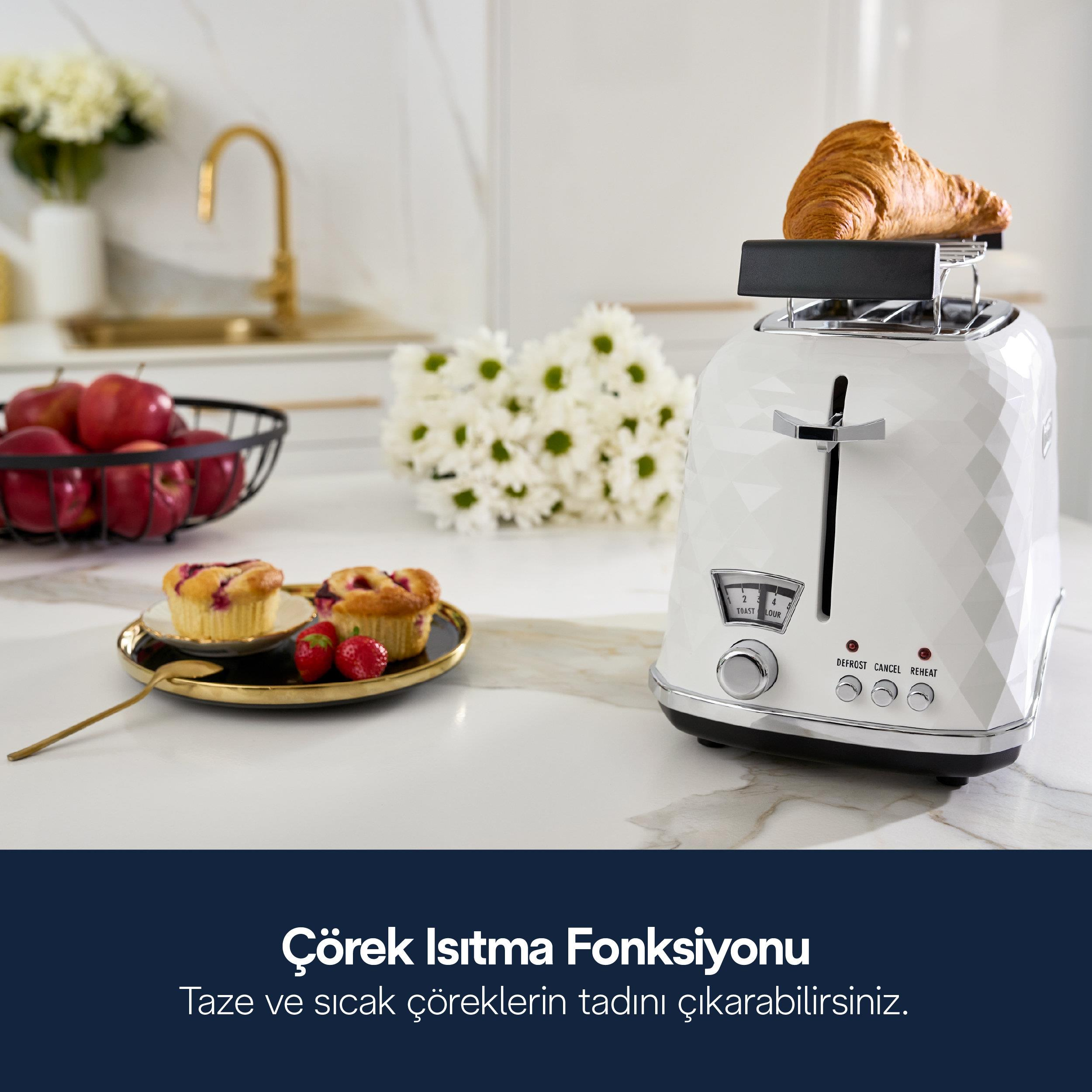 Un tostapane bianco con un croissant sopra si trova su un bancone di marmo con dolci, frutta e fiori.