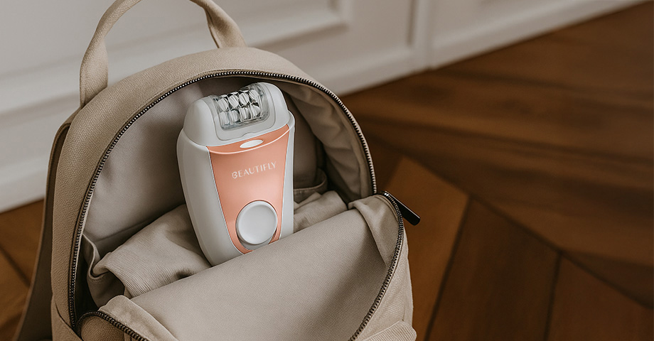 Biały i miedziany epilator w otwartym beżowym plecaku na drewnianej podłodze.
