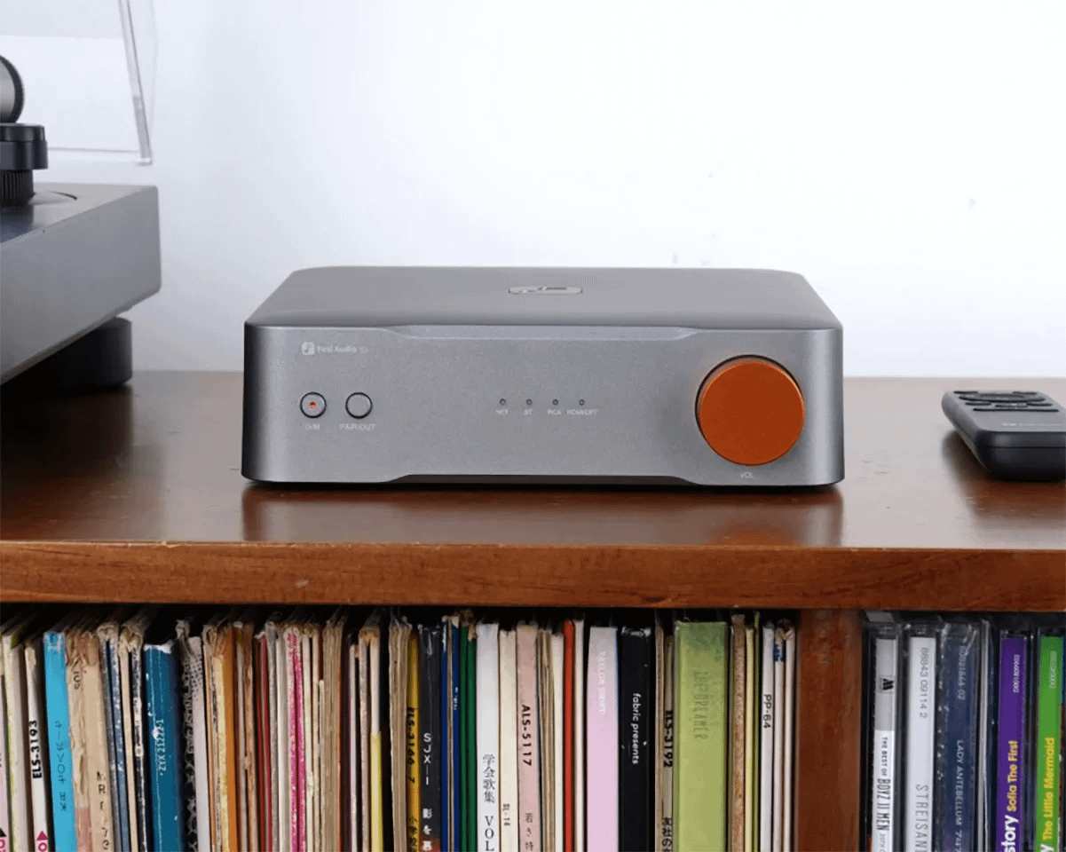 Un amplificador de audio gris con una perilla naranja está sobre un estante de madera.