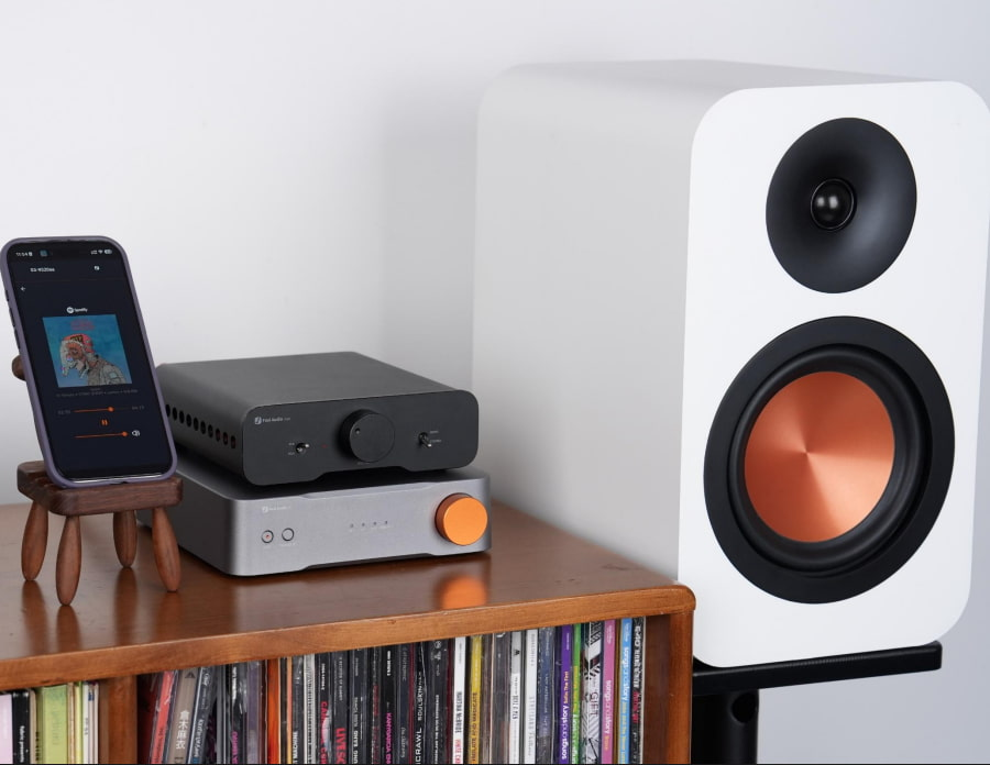 Teléfono inteligente, dos amplificadores de audio y un altavoz blanco con cono de cobre en un estante.