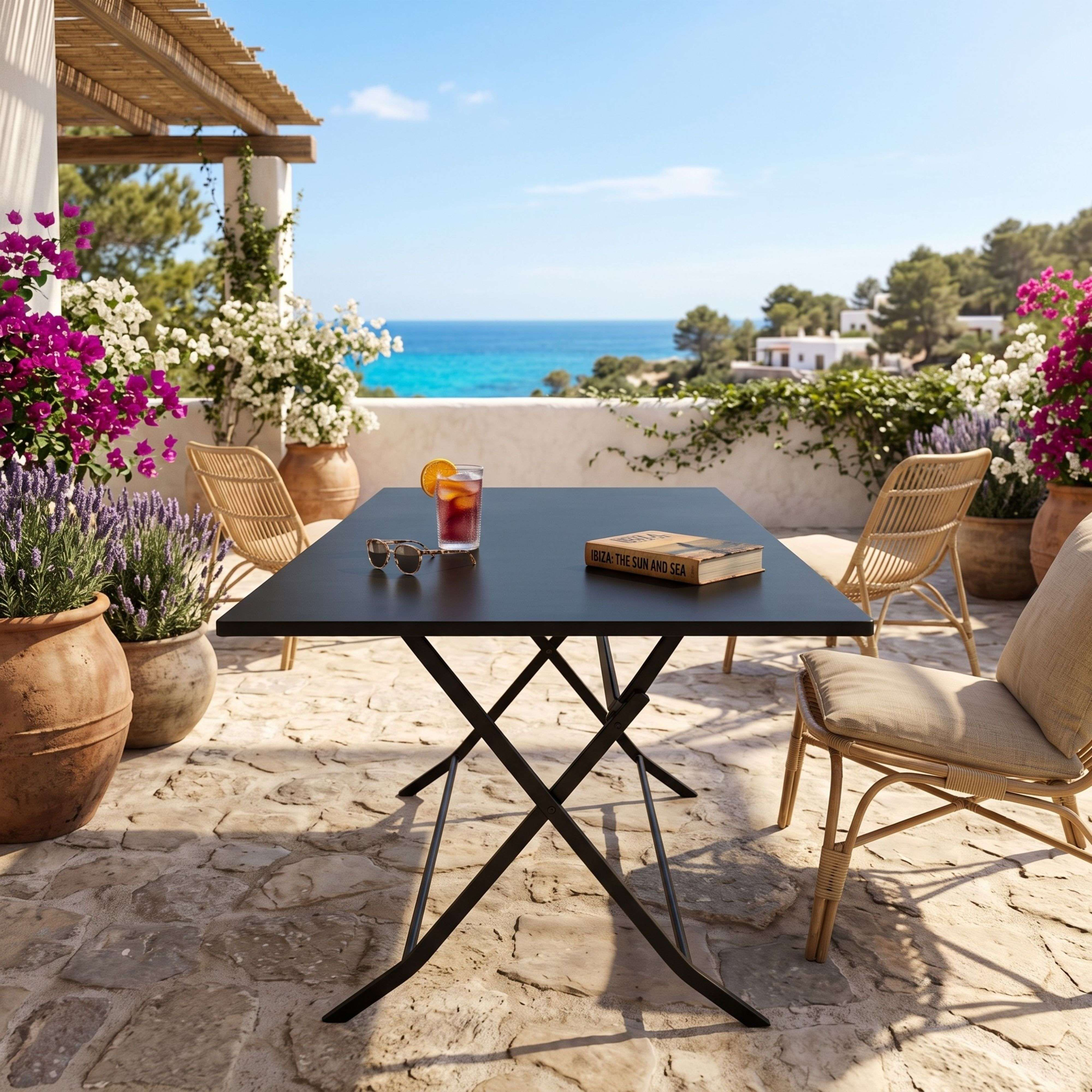 Mesa de patio con libro, gafas de sol y bebida con vista al mar.