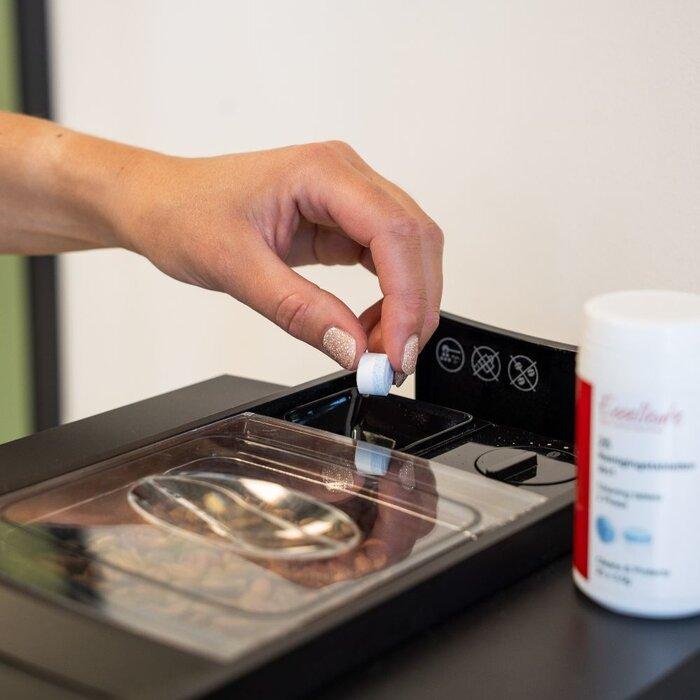 A hand places a cleaning tablet into the compartment of a coffee machine.