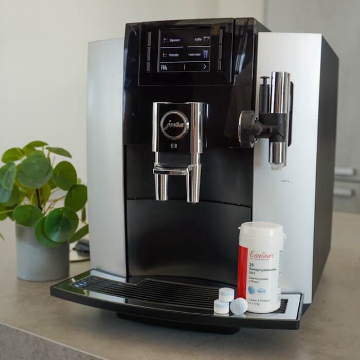 Modern coffee machine with cleaning tablets and potted plant on a counter.