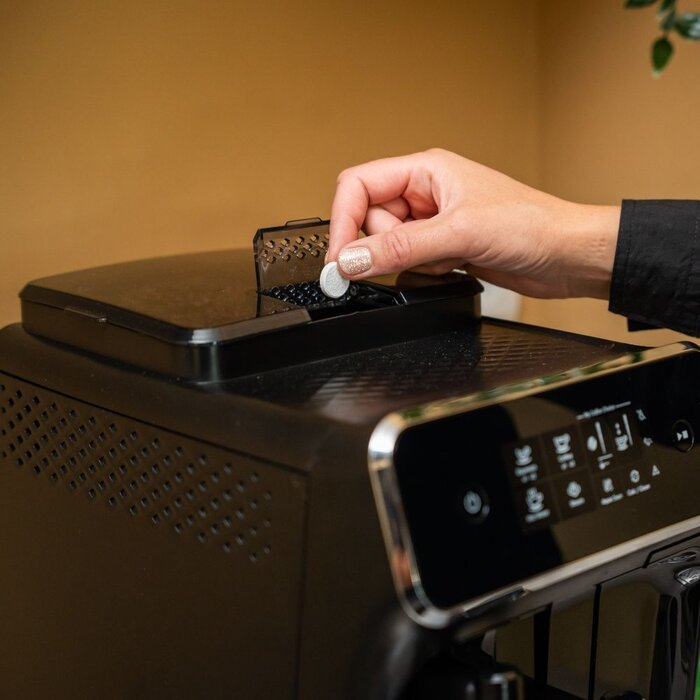 Een hand plaatst een reinigingstablet in het koffiekanaal van een machine.