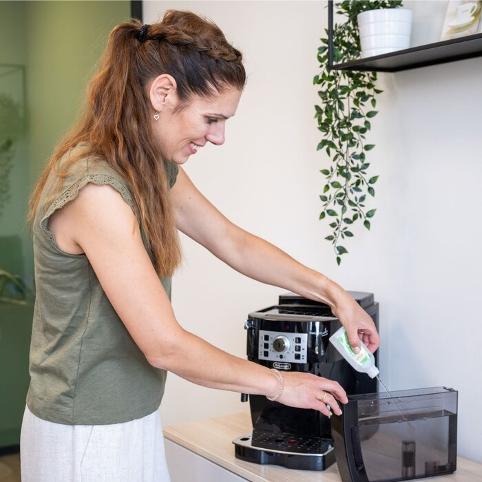 A woman in a green top pours liquid into a coffee machine water tank.