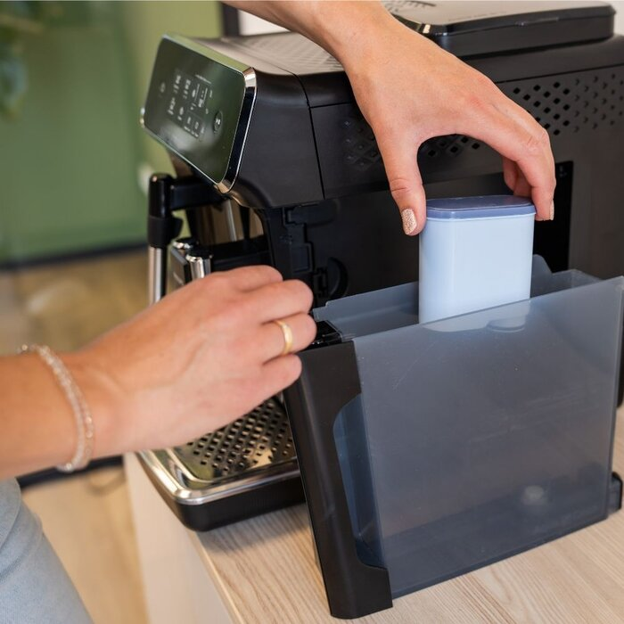 A person inserts a water filter into the water tank of a coffee machine.