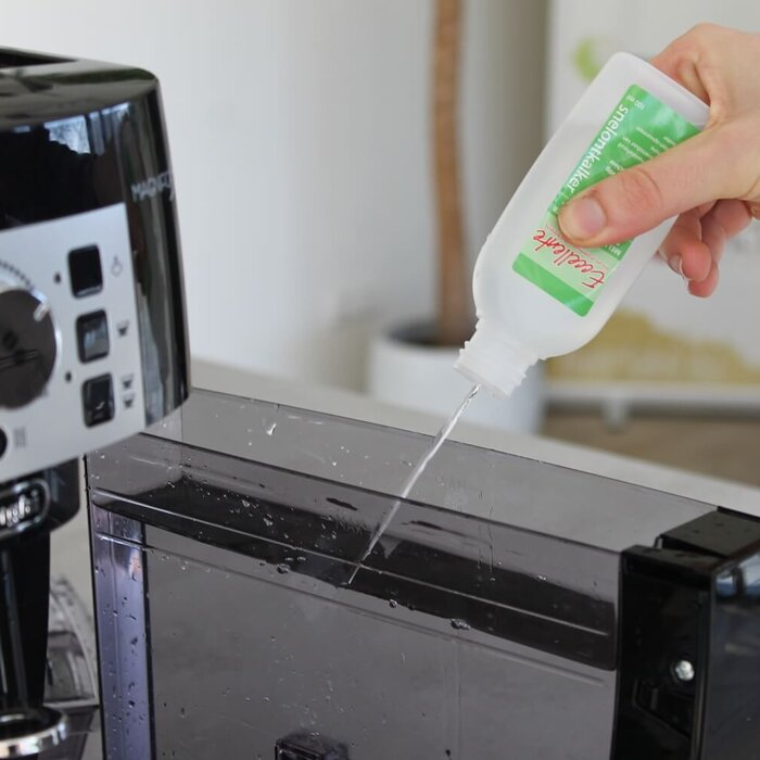 Iemand giet vloeistof uit een witte fles in het waterreservoir van een koffiezetapparaat.
