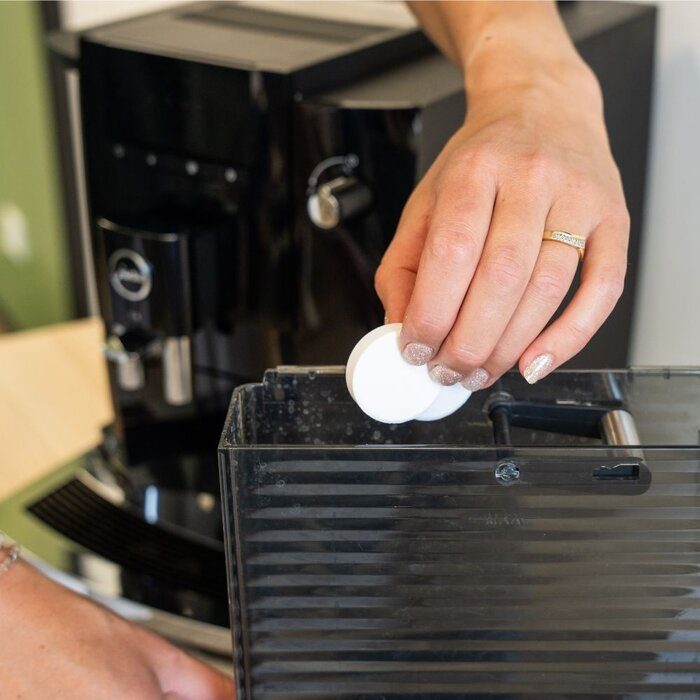 Een hand plaatst reinigingstabletten in het waterreservoir van een koffiemachine.