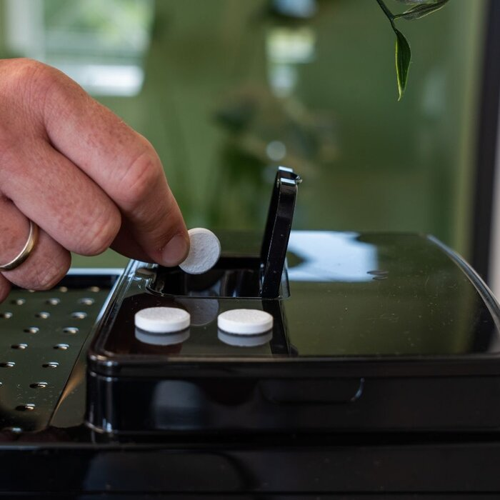 Hand plaatst witte tablet in koffiemachine met open vak.