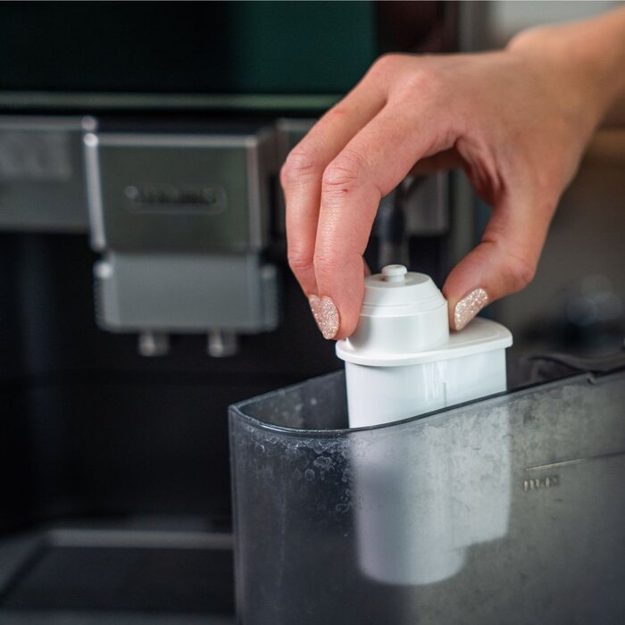 Une main insère un filtre à eau blanc dans le réservoir d'une cafetière.