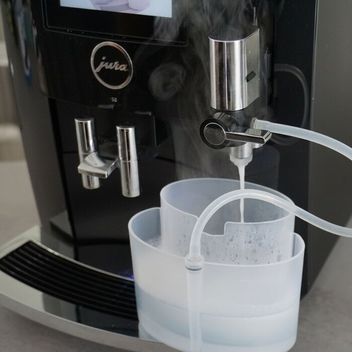 Een Jura-koffiezetapparaat reinigt zichzelf, water stroomt in een plastic container en stoom stijgt op.