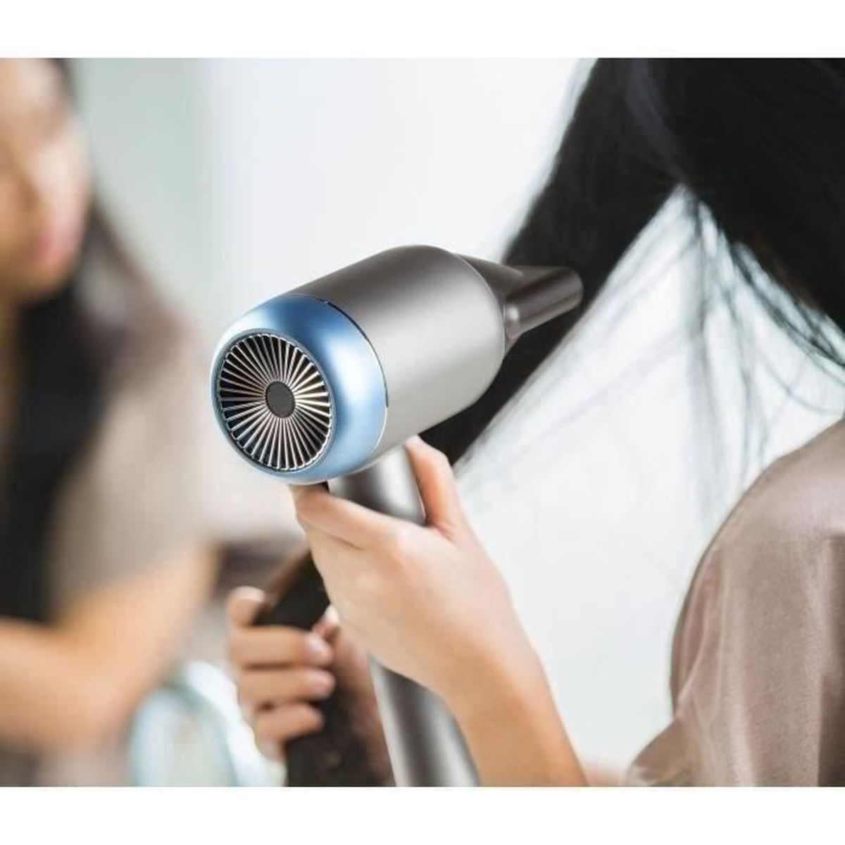 Una donna tiene in mano un moderno asciugacapelli grigio con anello blu, asciugandosi i capelli lunghi.
