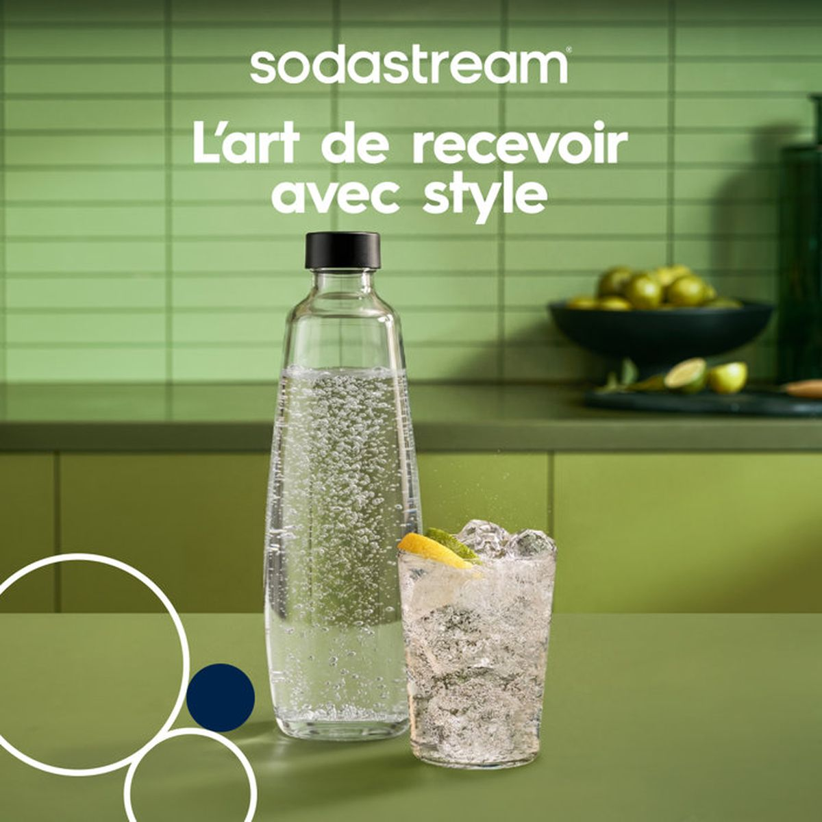 Una botella de cristal Sodastream con agua con gas y un vaso con hielo y limón en una encimera verde.
