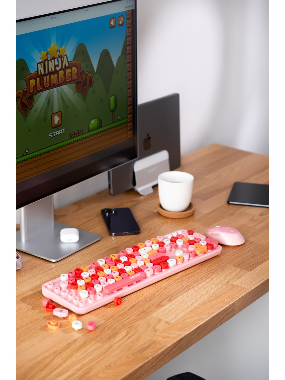Pembe klavye, fare, oyun gösteren monitör, telefon ve kahve fincanı olan bir masa.