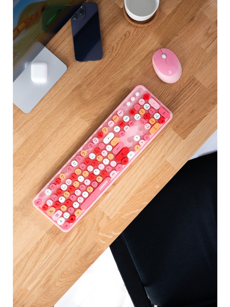 Ahşap bir masada pembe klavye, pembe fare, akıllı telefon, kulaklık ve bir monitör bulunmaktadır.