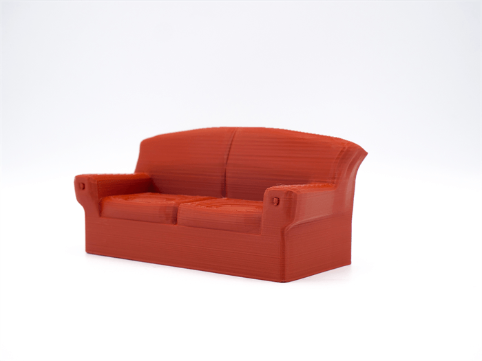 Un pequeño modelo de sofá rojo impreso en 3D se encuentra centrado sobre un fondo blanco.