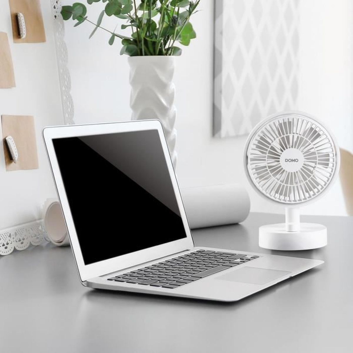 Un computer portatile, un vaso bianco con piante e una piccola ventola da scrivania su un tavolo grigio.