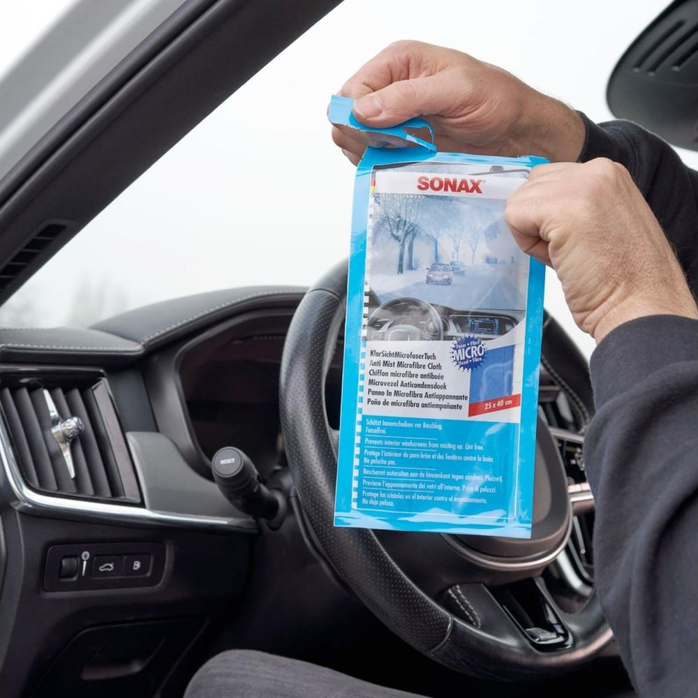 Personne ouvrant un paquet de chiffon anti-buée Sonax dans une voiture, devant le volant.