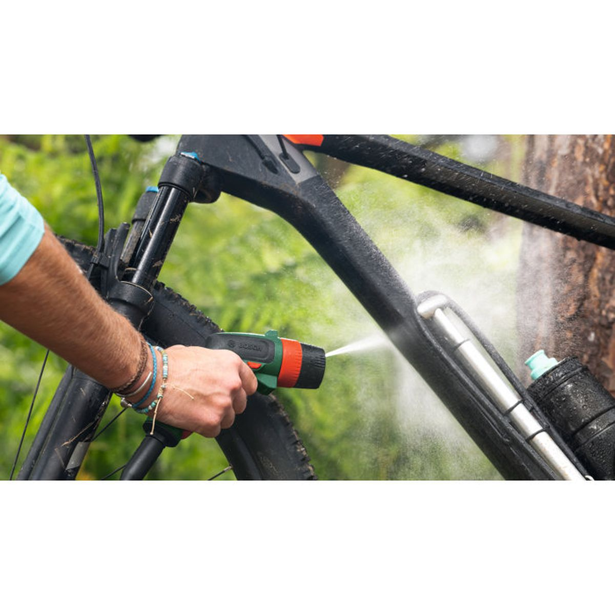 Une personne utilise un nettoyeur haute pression portatif pour nettoyer un VTT noir boueux à l'extérieur.