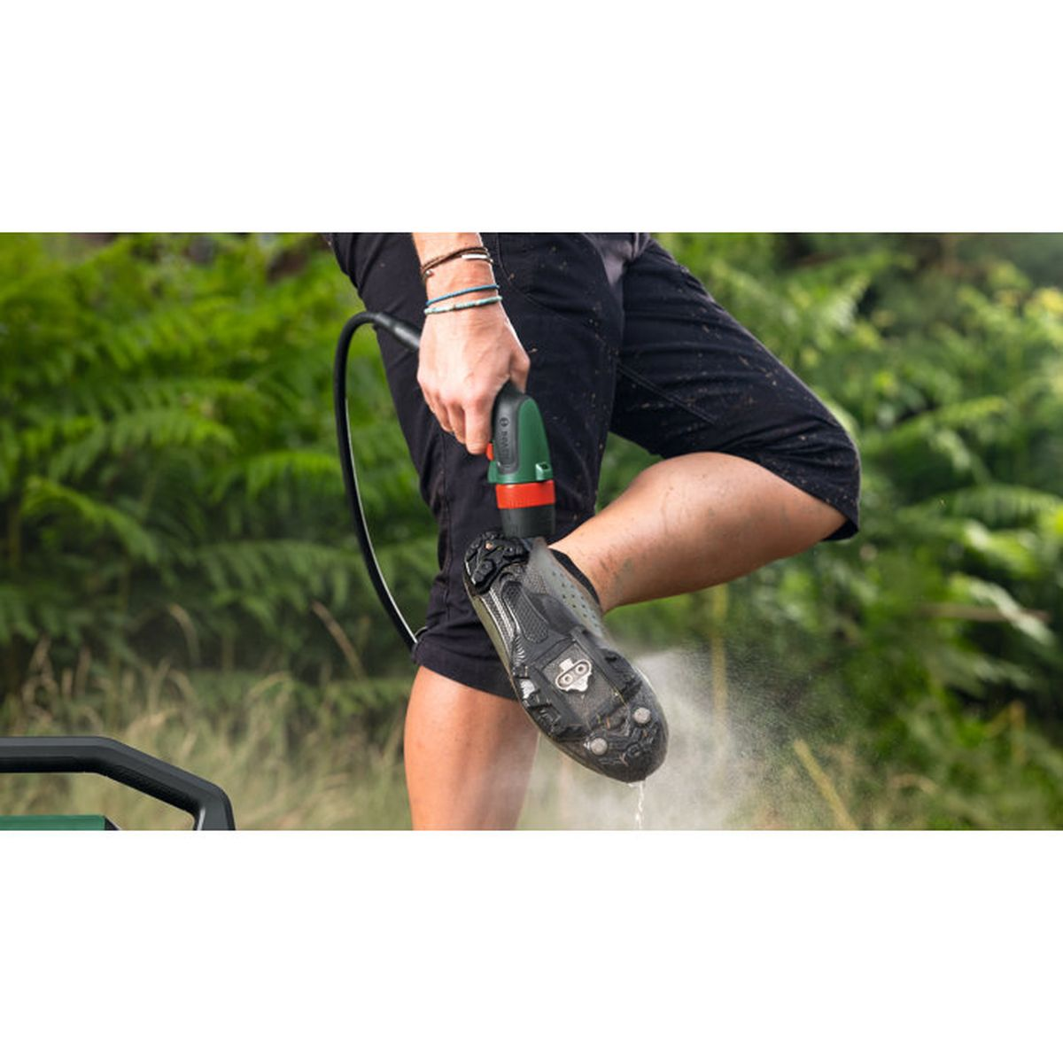 Une personne nettoie une chaussure de vélo boueuse avec un nettoyeur haute pression portable à l'extérieur.