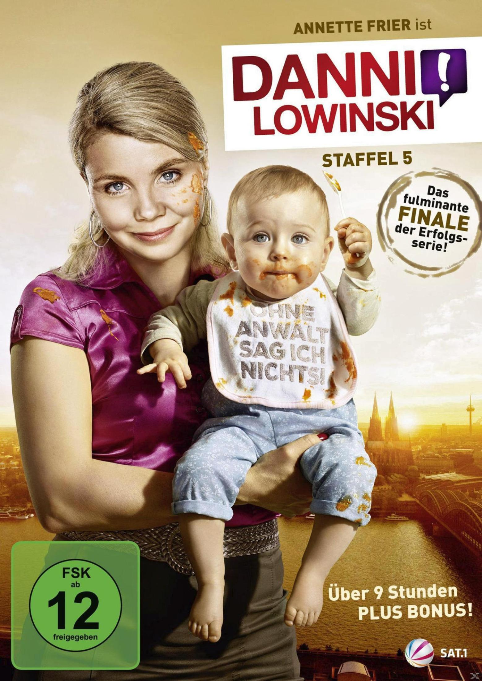Eine Frau hält ein Baby mit Lätzchen auf dem Arm, beide Gesichter sind mit Essen verschmiert, im Hintergrund Köln.