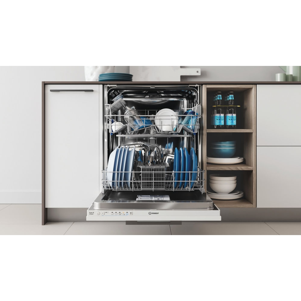 Una lavastoviglie bianca aperta con piatti blu, bicchieri e posate, installata sotto un moderno piano cucina.