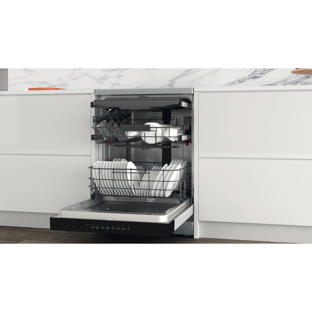 Lavastoviglie aperta in cucina bianca, piena di piatti puliti nei cestelli.