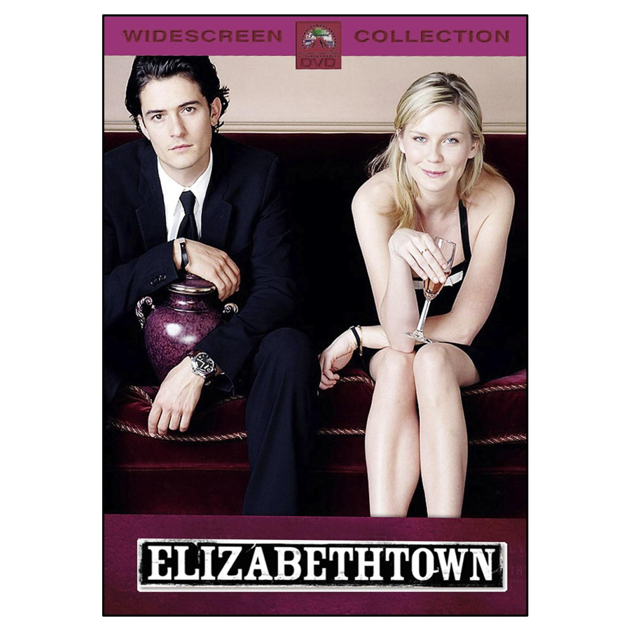 Ein Mann im Anzug mit einer Urne und eine blonde Frau mit einem Glas sitzen auf einem roten Sofa, für die Elizabethtown DVD.