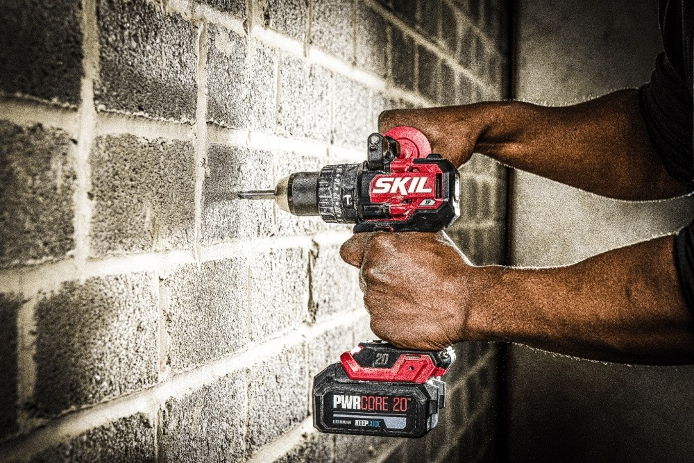 Una persona che fora un muro di mattoni usando un trapano a batteria SKIL rosso.