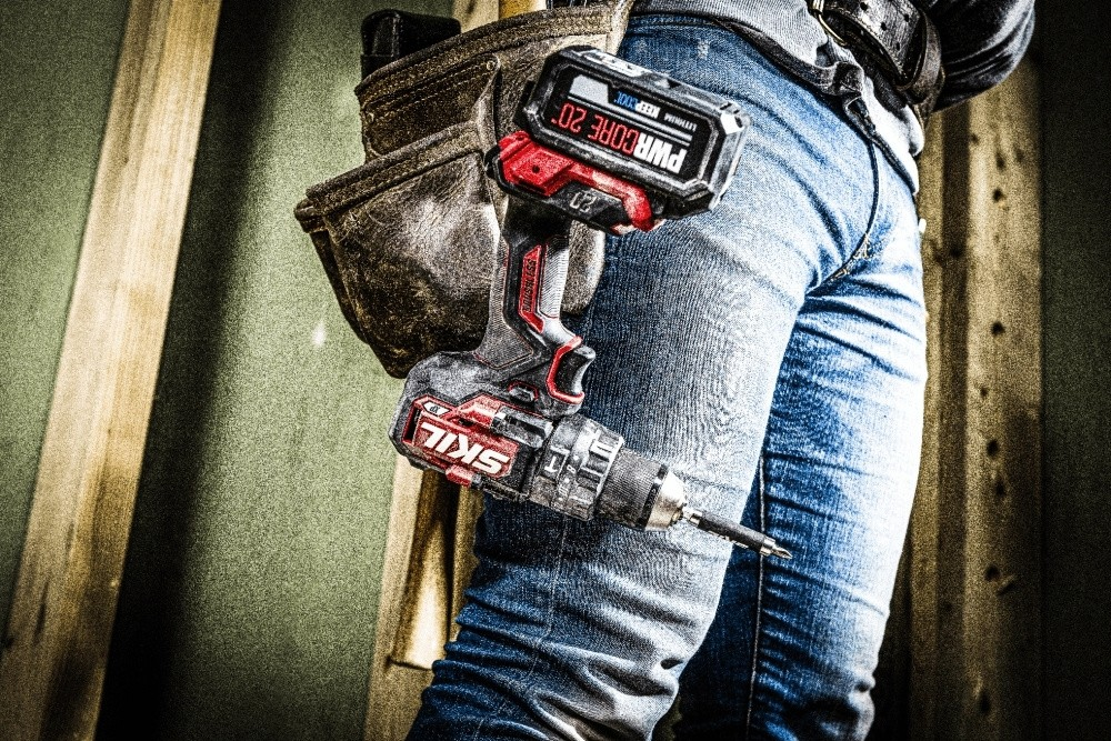 Un operaio in jeans e cintura porta attrezzi tiene in mano un trapano a batteria rosso e nero.